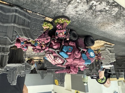 A pink-armoured transport and dreadnought move through grey ruins