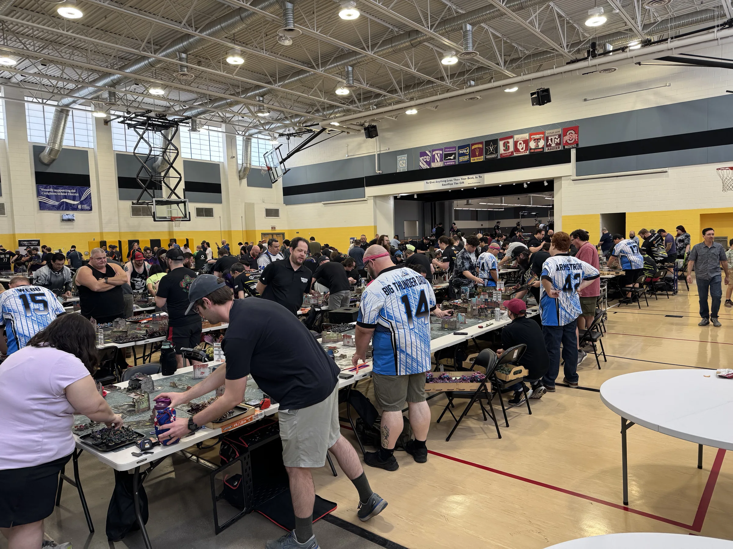 Players compete across rows of tabletop battlefields at a Smite Club major